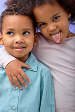 Two Cheerful Black Sister And Brother Having Fun While Standing Isolated Over Purple Background, Portrait Of Black Children In Casual Clothes Laughing, Smiling Together. Girl Is Showing Tongue