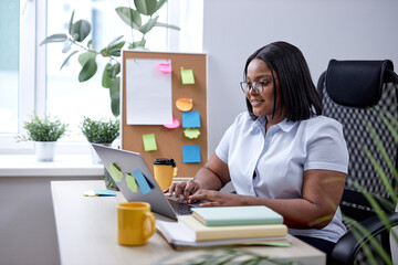 Wall Mural - pretty black lady typing on laptop keyboard working online in cozy modern office. american lady with black hair and skin enjoy working alone, managing. startup business. at workplace