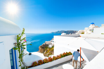 A young adult male traveler enjoys a private terrace patio at a luxury resort overlooking the sea on a sunny summer day in Oia, Santorini, Greece.