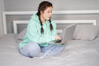© OliaVesna - remote working or distant studying from home. young brunette woman girl on bed with laptop. quarantine restrictions. covid-19 pandemic.