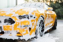 Cropped Image Of Wheel Of Luxury Yellow Car In Outdoors Self-service Car Wash, Covered With Cleaning Soap Foam.