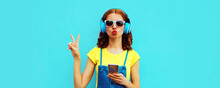 Portrait Of Young Woman In Headphones Listening To Music With Phone On Blue Background