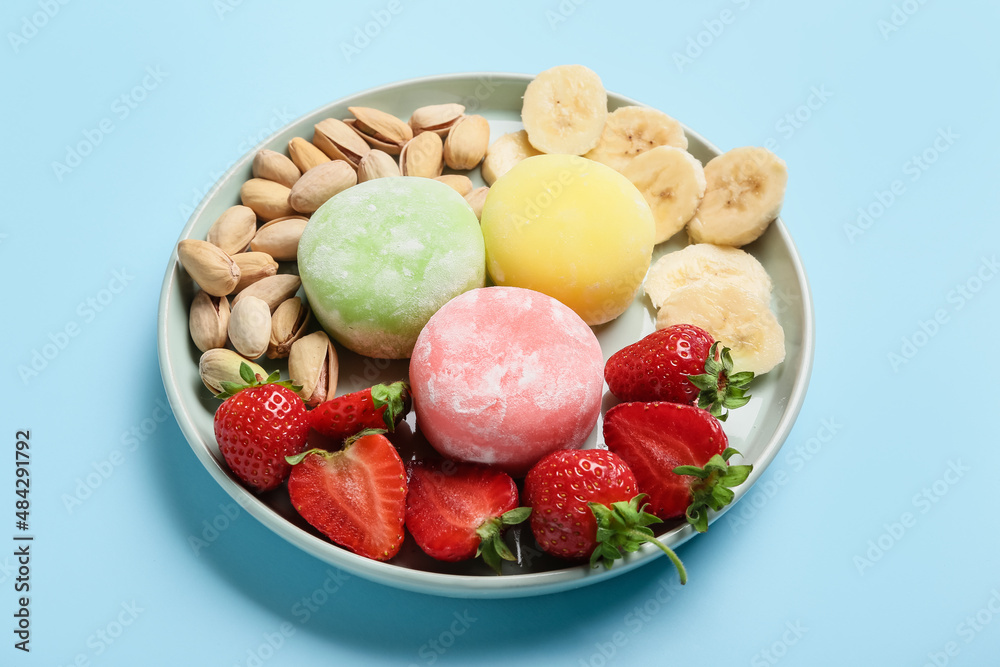 Plate with delicious mochi, fruits and nuts on color background