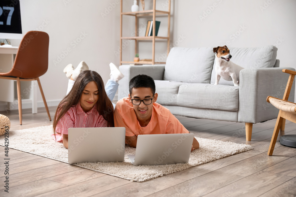 Young man with his wife using laptops on floor at home