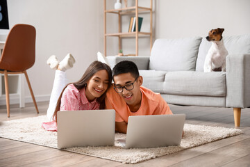 Wall Mural - Young man with his wife using laptops on floor at home