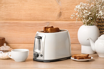 white toaster with bread slices, cup and vase on table near wooden wall