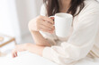 © lielos - 朝、自然光入る明るい部屋で温かい飲み物を飲む女性