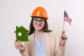 A girl in a construction helmet and an American flag holds a green eco house.