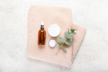 Jars with natural cosmetic cream, bottle of essential oil and towel on light background