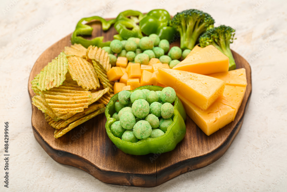 Wooden board with different snacks for St. Patrick's Day celebration on light background
