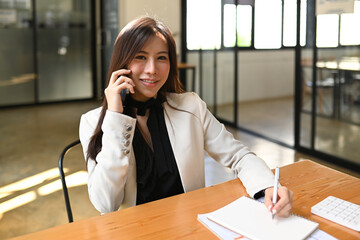 Wall Mural - Successful business woman talking on mobile phone while sitting in office.