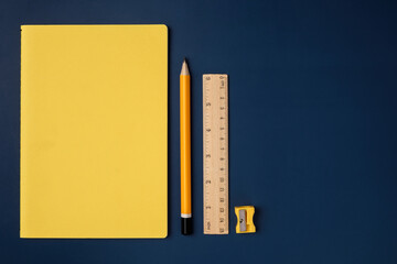 Poster - top view pastel yellow notebook with yellow pencil and notepad on navy blue working table