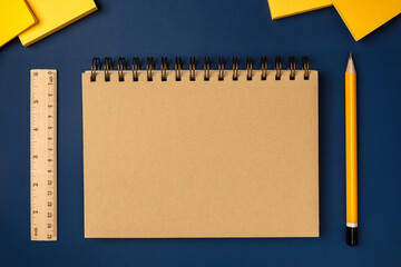 Poster - top view brown notebook with yellow pencil and notepad on navy blue working table
