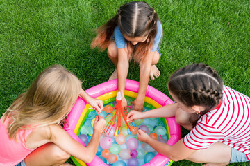 Summer fun outdoor activities for children concept. Top view of girls filling up water balloons at sunny day. Water balloon games for kids.