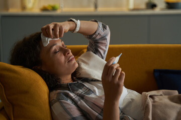 Female having an illness checking her temperature with thermometer