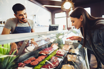 Butcher's shop seller helps to choose product to woman customer