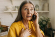 © shurkin_son - Indoor close-up image of shocked senior woman, having frightened and worried face expression after hearing bad news while talking on phone with her relatives standing against kitchen background