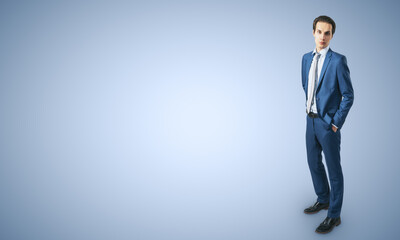 Poster - Job and recruiting concept with young businessman in blue classic suit, his hands in pockets on abstract light blue background with a space for your logo or text. Mockup