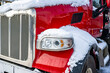 Shiny red big rig semi truck tractor standing for truck driver rest on the winter truck stop parking lot with snow and ice