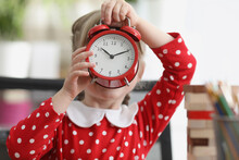 Little Girl Holding Red Alarm Clock In Front Of Her Face