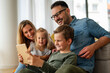 © NDABCREATIVITY - Happy young family having fun time at home. Parents with children using digital device.