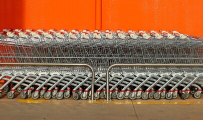 Row of shopping carts against a bright orange wall. Side view.