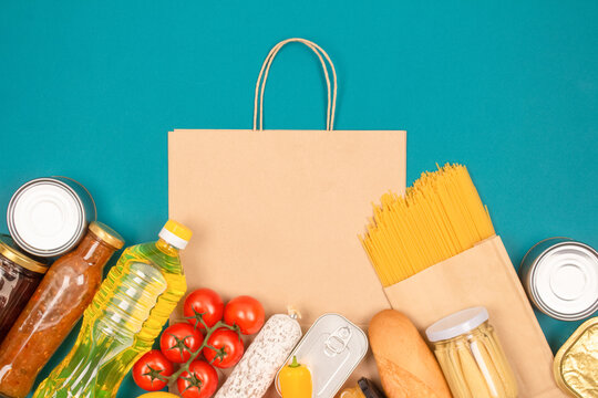 Food bank, food delivery concept. Paper bag with food donations on green background with copy space - pasta, fresh vegatables, canned food, baguette and other groceries. Mockup image