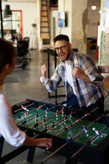 Colleagues having fun at work. Businessman and businesswoman playing table soccer..