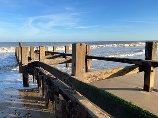 Wall Mural - Landscape of coastal barrier on sandy beach to protect from erosion with wood platform into sea water on fresh bright day with blue sky and low waves in Winter at Gorleston Norfolk East Anglia uk