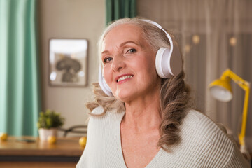 elderly woman in headphones listens to music, sings and dances at home in the evening. seniors llifestyle. Audio healing. 