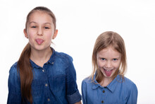 Two Kid Girls 6 And 8 Years Old With Wide Open Mouth And Shows Tongue And Grimaces. Child Wearing A Denim Dress Face Expression Over White Background