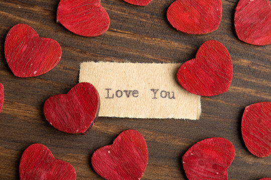 Love you - typed text. Valentines Day greetings concept. Little red wooden hearts close up. Valentines greeting card.