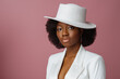 Elegant beautiful African American woman wearing classic white blazer, stylish fedora hat, posing in studio, on pink background. Close up portrait. Copy, empty space for text
