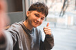 © morrowlight - Smiling gen Z teenage boy 17-18 year old show thumb up to camera and make selfie closeup. Happy millennial man with blonde hairstyle. Happiness.