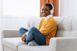 © anatoliycherkas - Rest And Relax Concept. Calm black woman sitting on bean bag, listening to music, audio book, podcast, enjoying meditation for sleep and peaceful mind in wireless headphones, leaning back, copy space