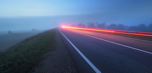 Wall Mural - Panoramic view of the empty highway through the fields in a fog at night. Moonlight. Sunrise. Europe. Transportation, logistics, travel, road trip, freedom, driving. Motion blur effect. Rural scene