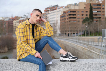 Wall Mural - Non binary person sitting on a wall with a book with a blank look on his face.