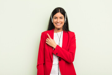 Wall Mural - young pretty hispanic woman smiling cheerfully, feeling happy and pointing to the side. telemarteker concpet