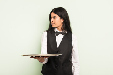 Wall Mural - young pretty hispanic woman on profile view thinking, imagining or daydreaming. waiter with tray concept