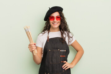 Wall Mural - young pretty hispanic woman smiling happily with a hand on hip and confident. artist concept