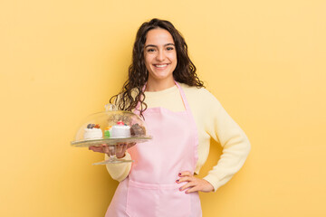 Wall Mural - young pretty hispanic woman smiling happily with a hand on hip and confident. chef and cakes concept