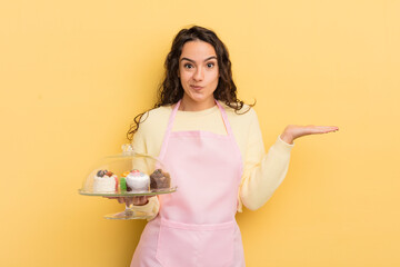 Wall Mural - young pretty hispanic woman feeling puzzled and confused and doubting. chef and cakes concept