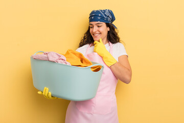 Wall Mural - young pretty hispanic woman smiling with a happy, confident expression with hand on chin. wash and clothes concept