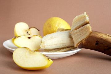 Wall Mural - Shriveled yellow apples and overripe banana on a white plate. One apple is crushed into pieces. Selective focus. Light brown background