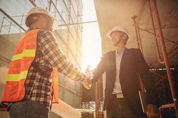 Wall Mural - Architect and engineer construction workers shaking hands while working at outdoors construction site. Building construction collaboration concept