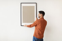 Young Man Hanging Picture Frame On The Wall