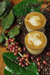 2 cups of hot coffee latte art with heart and leaf on wooden table with roasted arabica coffee beans and red cherry coffee beans concept.