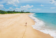 © Soloviova Liudmyla - Young female dressed in light summer clothes walking barefoot leaving footprints on the sand on Indian ocean Tangalle lonely coconut trees beach on Sri Lanka island. Aerial top view drone shot.