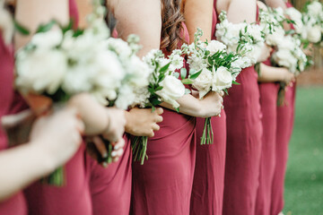 Wall Mural - Bridesmaids in red dresses holding their wedding bouquets of flowers with white roses Closeup of bridesmaids holding flowers at the wedding day holding flowers in hands Cropped photo