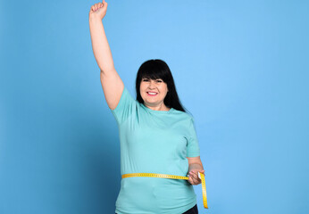 Wall Mural - Happy overweight mature woman measuring waist with tape on light blue background